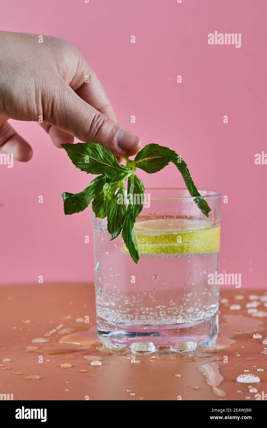 Ein Glas kalte erfrischende Limonade auf rosa Hintergrund und Frau mit Minze Stockfoto