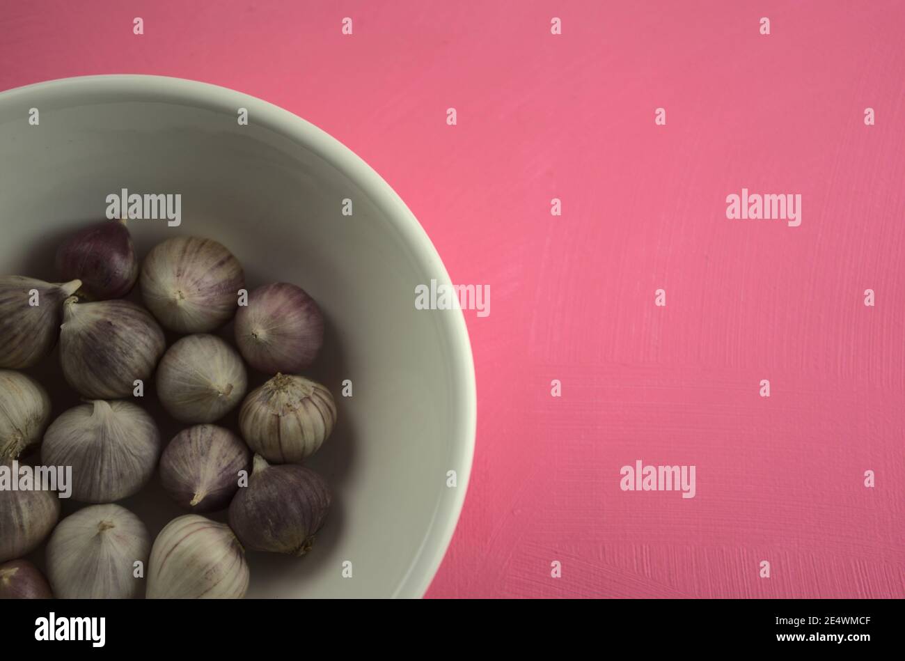 Knoblauch in Schüssel auf Acryl kratzende rosa Leinwand Hintergrund. Essen, Küche, Essen, Stillleben Fotografie mit Kopierraum. Stockfoto