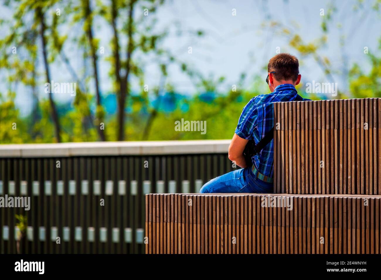 Ein junger und schöner Tausendjähriger Mann sitzt auf einer Bank im modernen Park in der Stadt. Rückansicht. Stockfoto