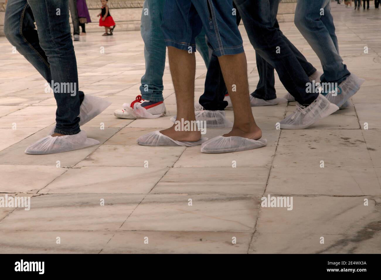 Eine Gruppe von jungen Besuchern, die zusammen auf weißem Marmorboden auf der Plattform des Taj Mahal mit Einweg-Socken auf. Stockfoto