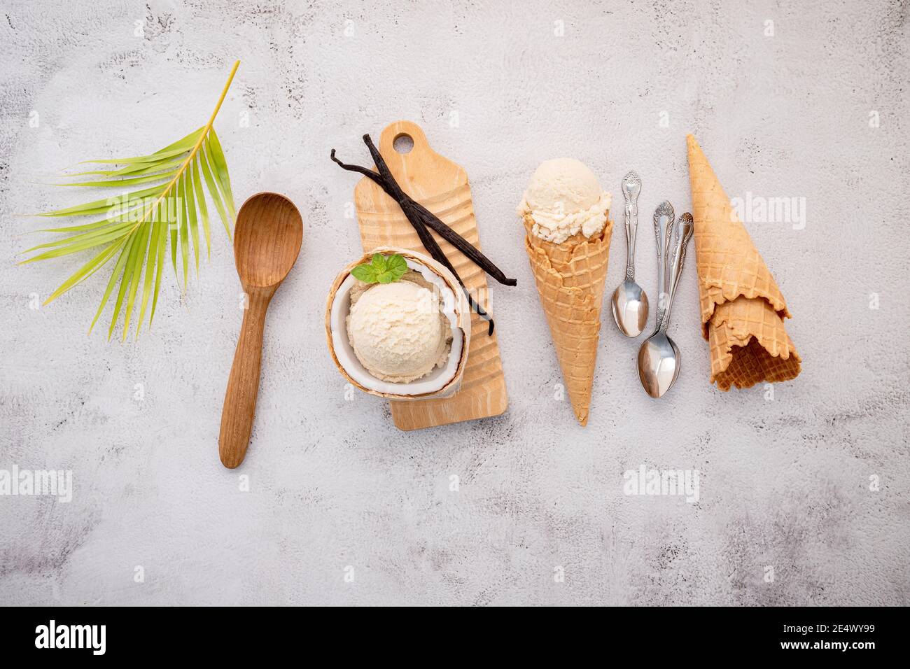 Kokoseis Aromen in der Hälfte der Kokosnuss Setup auf weißem Stein Hintergrund. Sommer und Süße Menükonzept. Stockfoto
