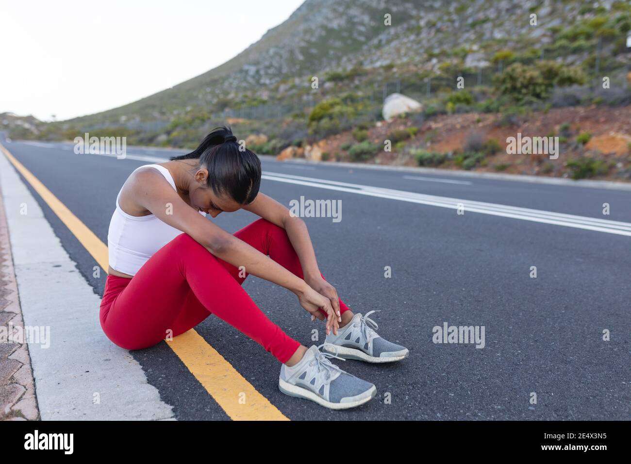 Fit afroamerikanische Frau in Sportswear sitzen und ruhen auf Eine Küstenstraße Stockfoto