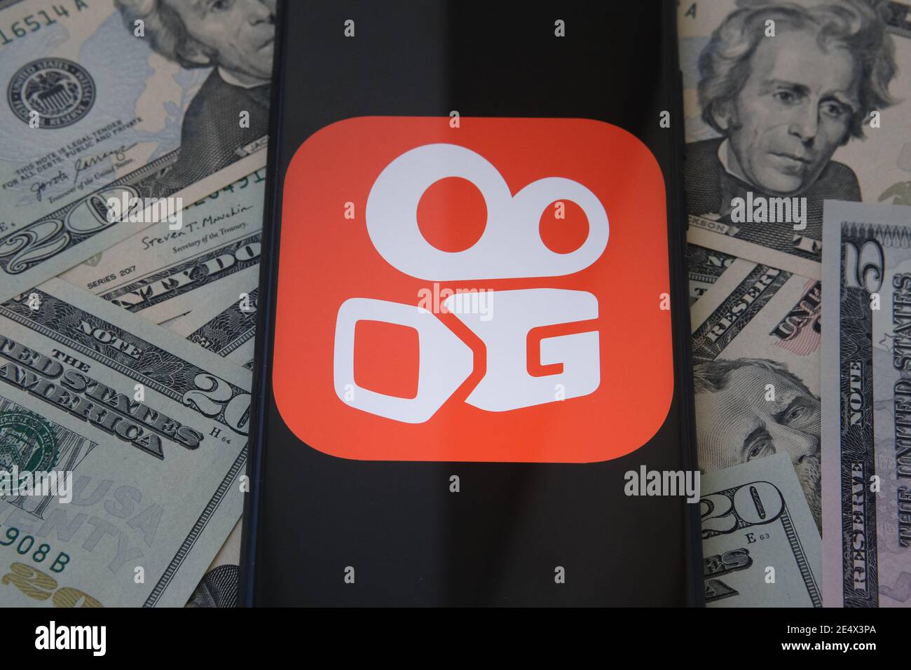 Stafford, Großbritannien - Januar 25 2021: Kuaishou App-Logo auf dem Smartphone-Bildschirm und verschwommene Dollar-Banknoten auf dem Hintergrund. Konzept für Stockfoto
