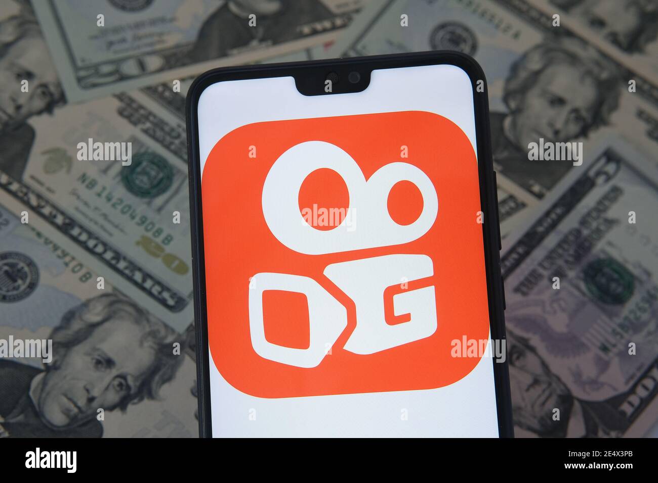 Stafford, Großbritannien - Januar 25 2021: Kuaishou App-Logo auf dem Smartphone-Bildschirm und verschwommene Dollar-Banknoten auf dem Hintergrund. Konzept für Stockfoto