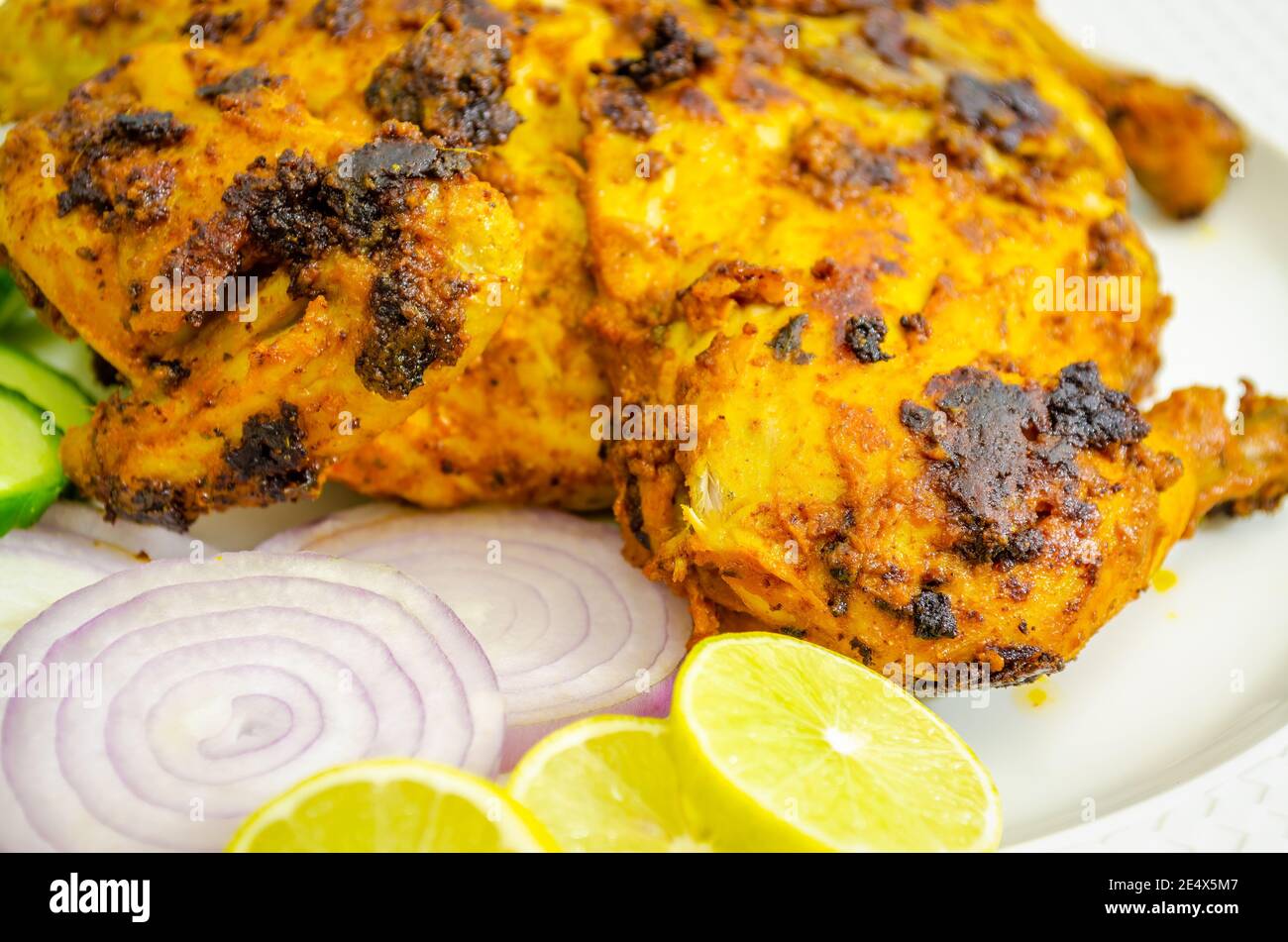 Nahaufnahme eines würzigen Tandoori-Hähnchens mit Zwiebeln, Zitrone und Gurke Stockfoto
