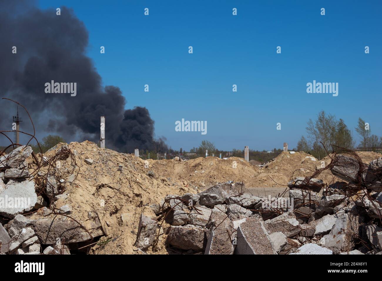 Die Betonschutt des Gebäudes mit Ziegeln und vorstehenden Armaturen auf einem Hintergrund von blauem Himmel mit dicken schwarzen Rauch. Hintergrund. Stockfoto