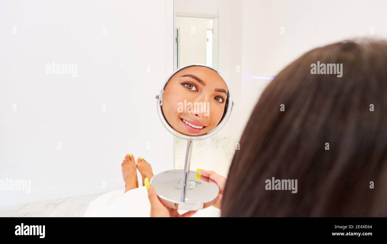 Eine junge Frau schaut in einem Kosmetikspiegel auf ihr Gesicht Nach einer Hautbehandlung Stockfoto