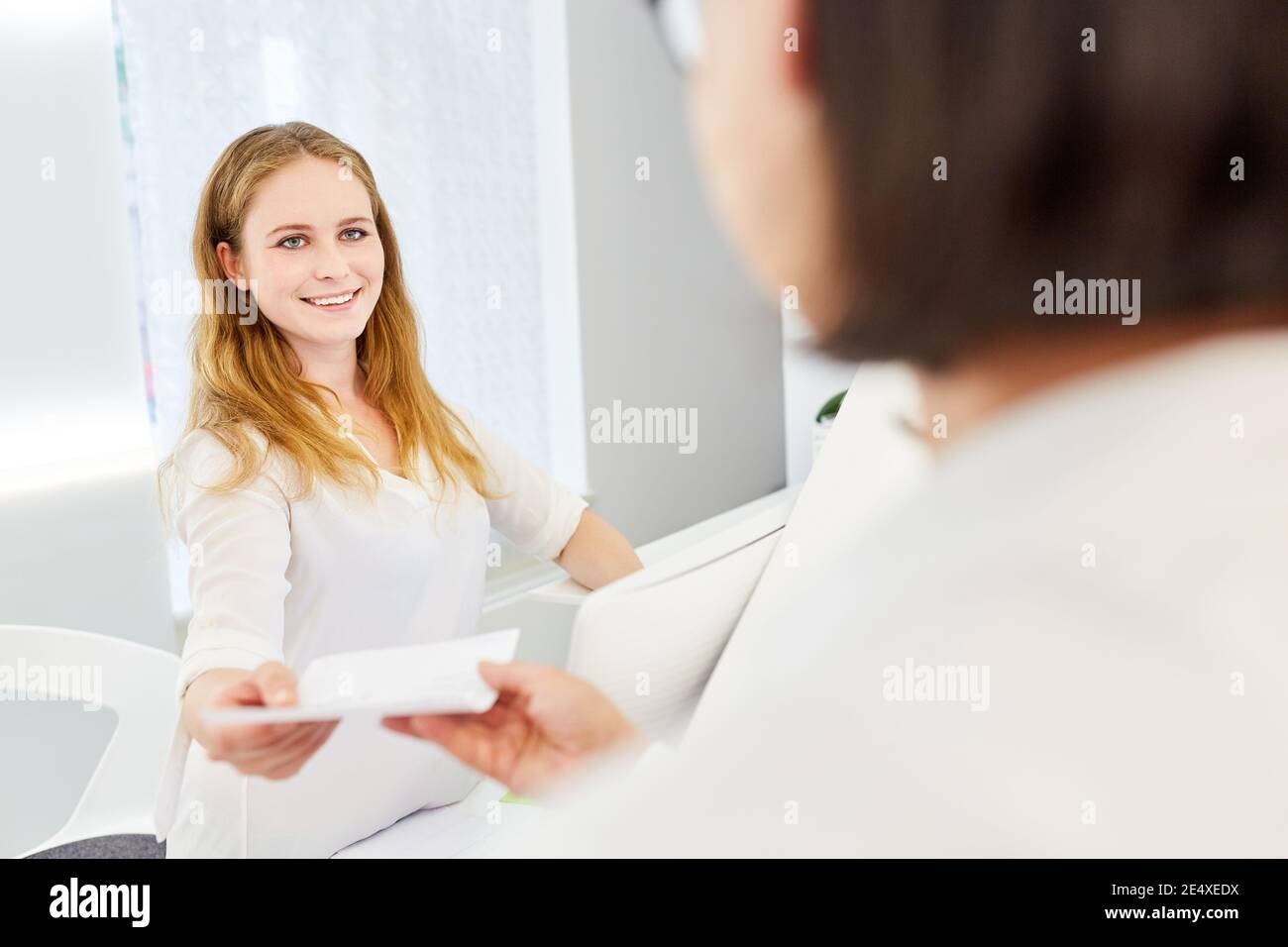 Junge Frau als Patientin mit einer Krankenversicherungsbescheinigung An der Rezeption in einer Arztpraxis Stockfoto