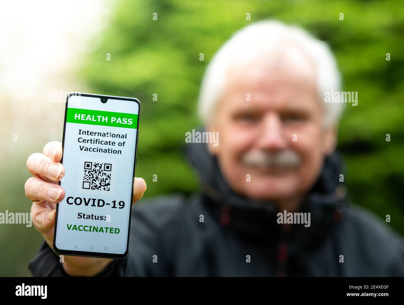 Älterer Mann zeigt einen Gesundheitsausweis auf einem Handy, was auf eine Impfung gegen covid-19 hinweist. Stockfoto