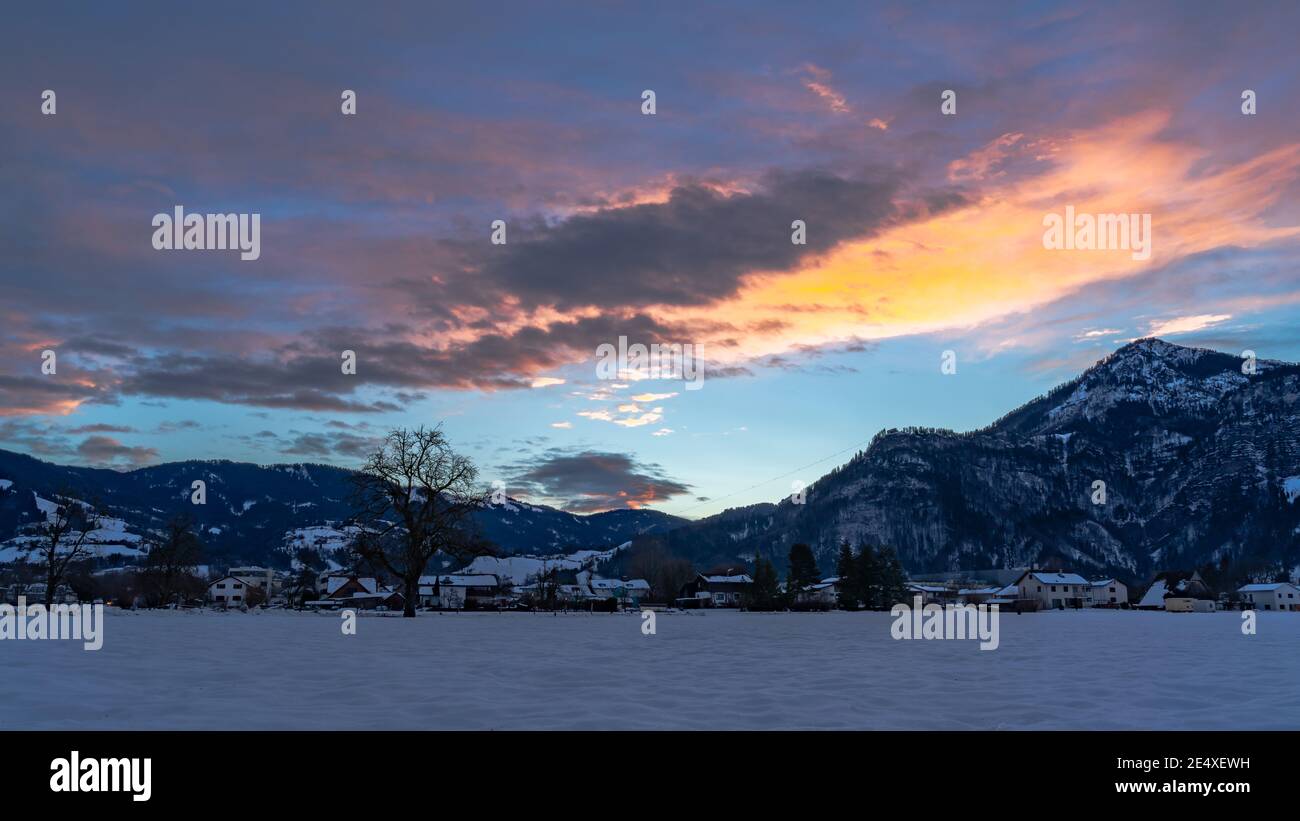 Zartfarbener Sonnenaufgang im Rheintal. Leuchtender Sonnenaufgang in Dornbirn, Vorarlberg, Österreich. Roter und orangefarbener Sonnenaufgang im Winter, mit Bäumen Stockfoto