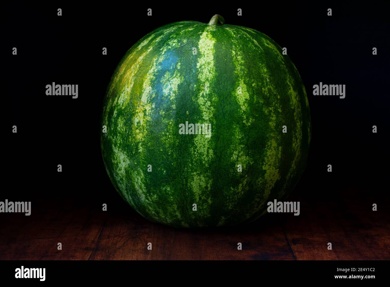 Wassermelonenfrucht liegt auf einem rustikalen Holzhintergrund. Diese saftige Schönheit taucht aus der dunklen und verbergenden erfrischenden Süße auf. Stockfoto