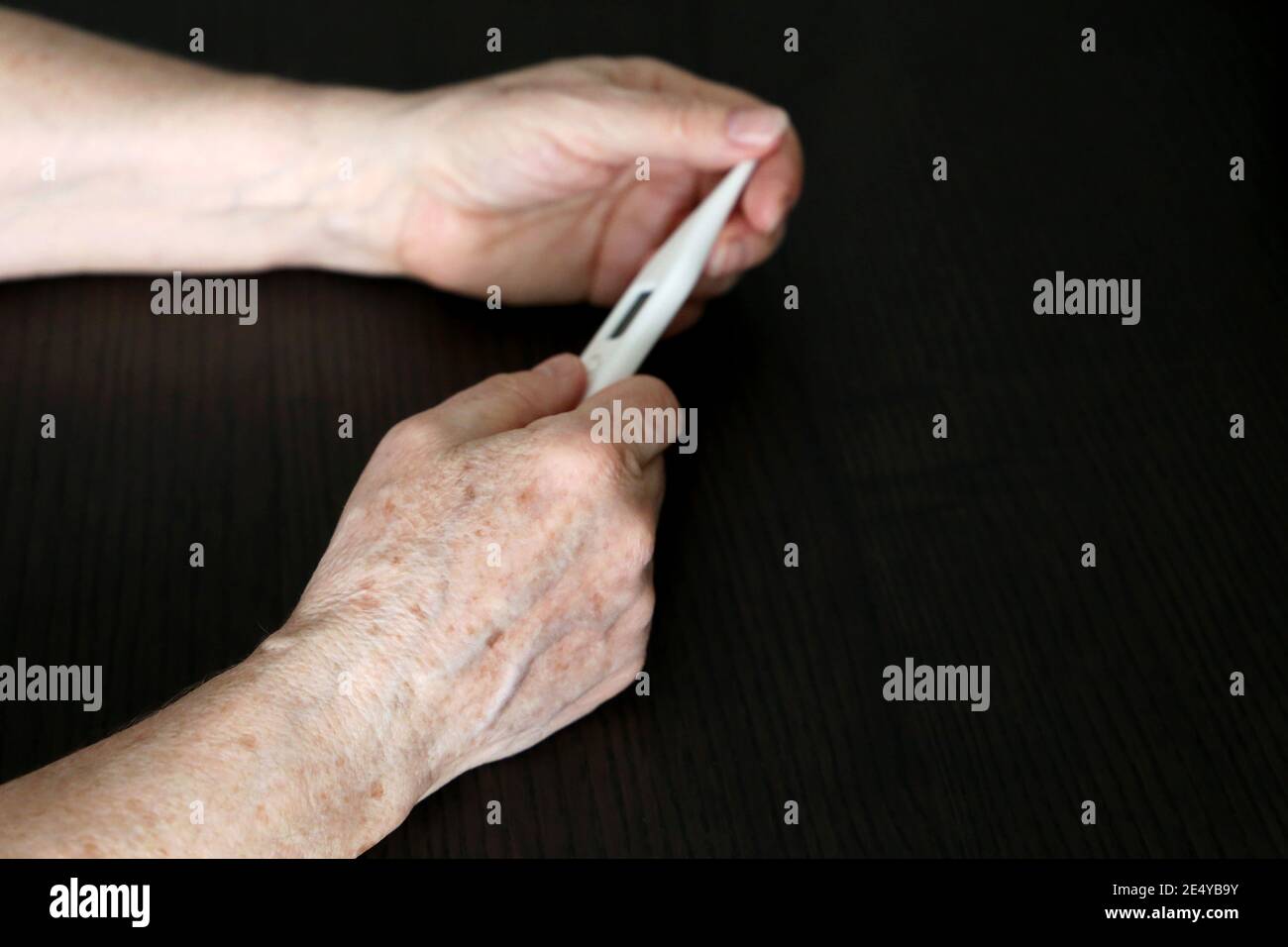 Ältere Frau misst Körpertemperatur, Konzept von Fieber, Coronavirus-Symptome. Digitalthermometer in faltigen weiblichen Händen aus der Nähe Stockfoto