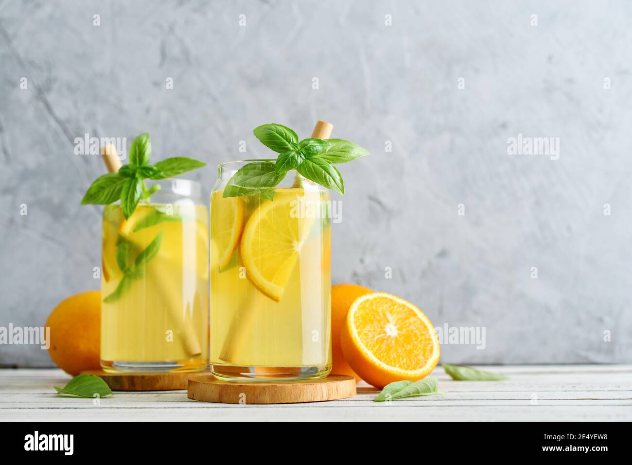Limonade mit Orange und Basilikum, kaltes Erfrischungsgetränk in Gläsern auf grauem Hintergrund Stockfoto