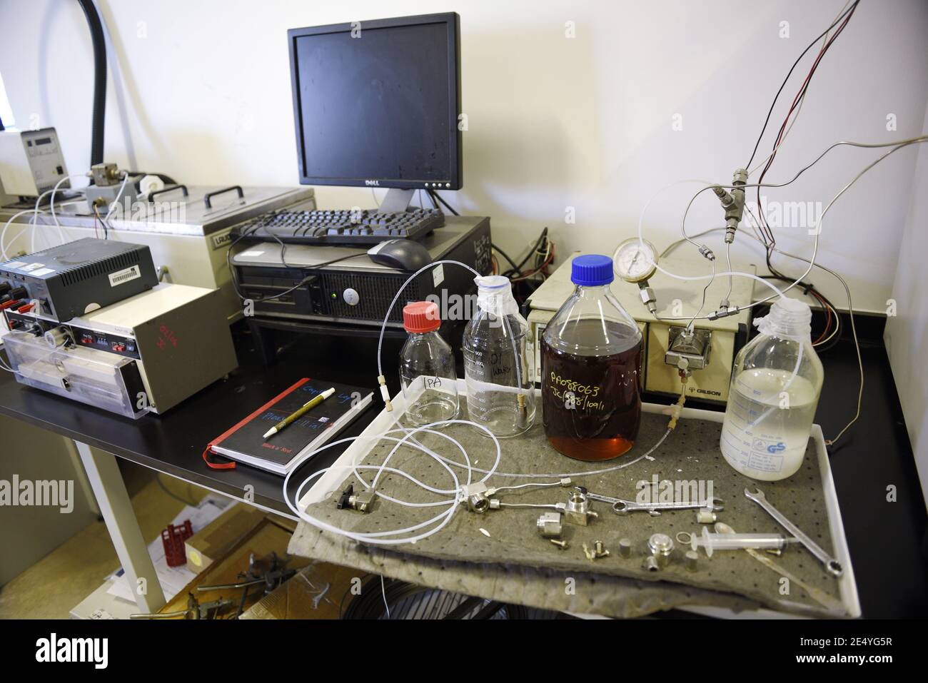 Arbeitsplatz in einem echten Wissenschaftslabor, ziemlich chaotisch. Einschließlich Computer, Notizblock, Stift, Probengefäße, Schraubenschlüssel und verschiedene Geräte auf einem Arbeitstisch. Stockfoto