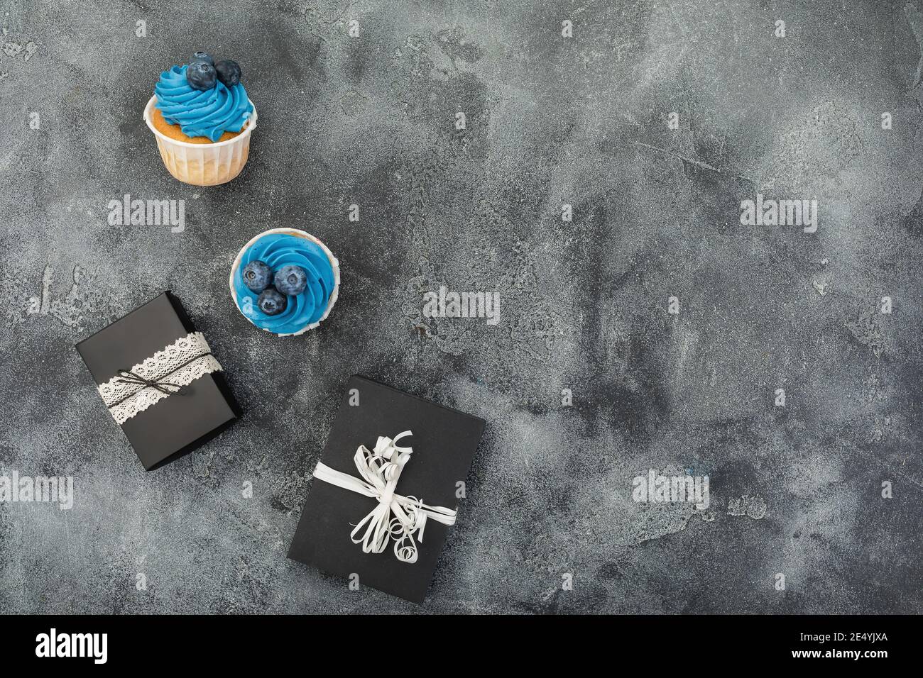 Muffins mit blauer Creme und Geschenk auf dunklem Hintergrund. Flach liegend, Draufsicht Stockfoto