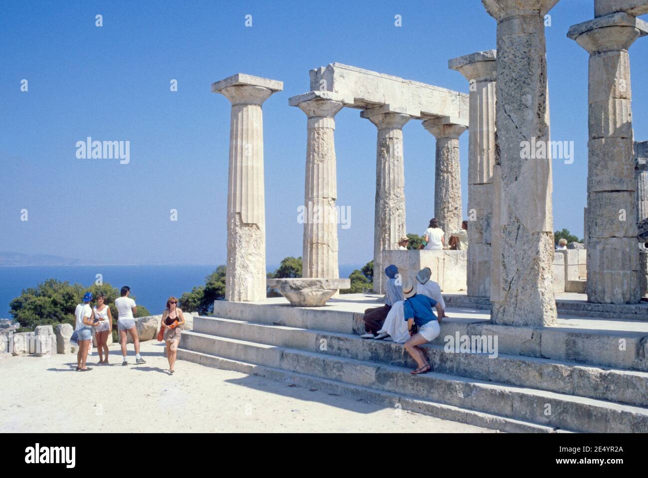 1986 Griechenland Tempel von Aphaia Aegina der Tempel von Aphaia oder Afea ist innerhalb eines Sanktuariums, das der Göttin Aphaia auf der griechischen Insel Aegina im Saronischen Golf gewidmet ist. Früher bekannt als der Tempel des Jupiter Panhellenius, ist der dorische Tempel jetzt als der Mutter-Göttin Aphaia gewidmet anerkannt, Touristen auf einer Führung genießen den Blick auf den griechischen Tempel, Ägina Griechenland EU Europa Stockfoto