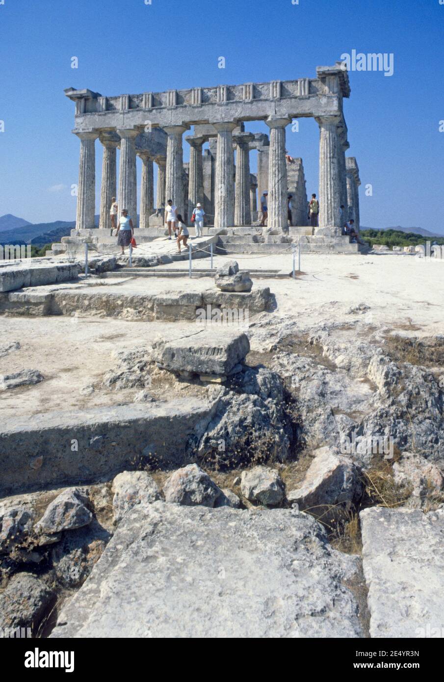 1986 Griechenland Tempel von Aphaia Aegina der Tempel von Aphaia oder Afea ist innerhalb eines Sanktuariums, das der Göttin Aphaia auf der griechischen Insel Aegina im Saronischen Golf gewidmet ist. Früher bekannt als der Tempel des Jupiter Panhellenius, ist der dorische Tempel jetzt als der Mutter-Göttin Aphaia gewidmet anerkannt, Touristen auf einer Führung genießen den Blick auf den griechischen Tempel, Ägina Griechenland EU Europa Stockfoto