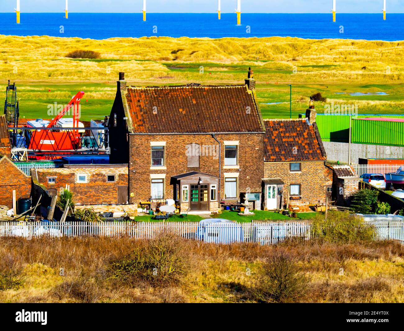 Das Marsh Farm House, das einst auf dem Marsch von Warrenby liegt, ist heute von Industrie umgeben und liegt auf dem Redcar Wind Farm und den Golfplätzen dahinter Stockfoto