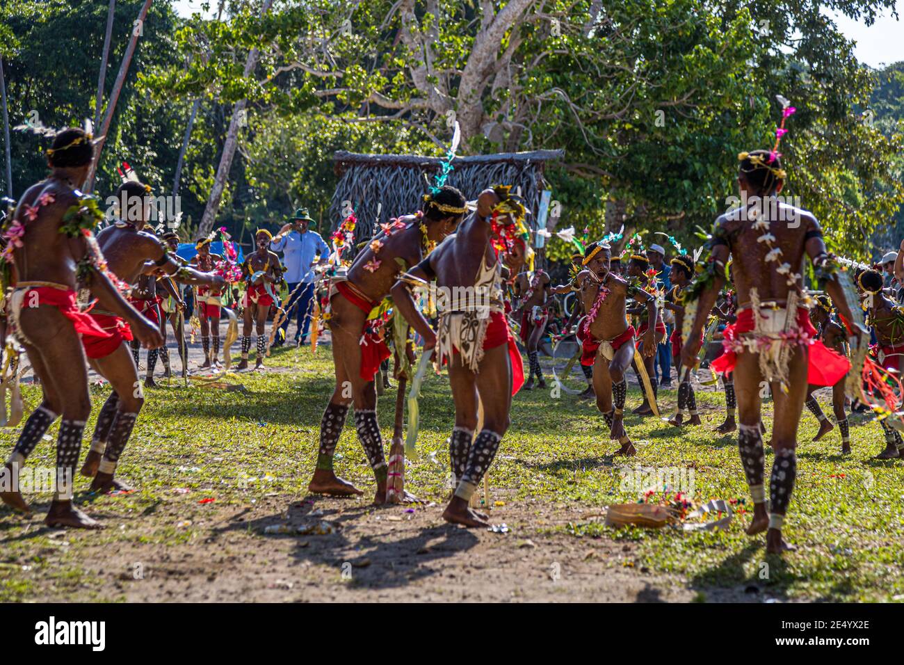 Kostümierte Tänzer, die hölzerne Stäbe halten, tanzen um das aus Stöcken gebaute Wicket während eines Cricketspiels im Stil der Trobriand-Inseln in Kwebwaga, Trobriand-Inseln, Papua-Neuguinea. Stockfoto