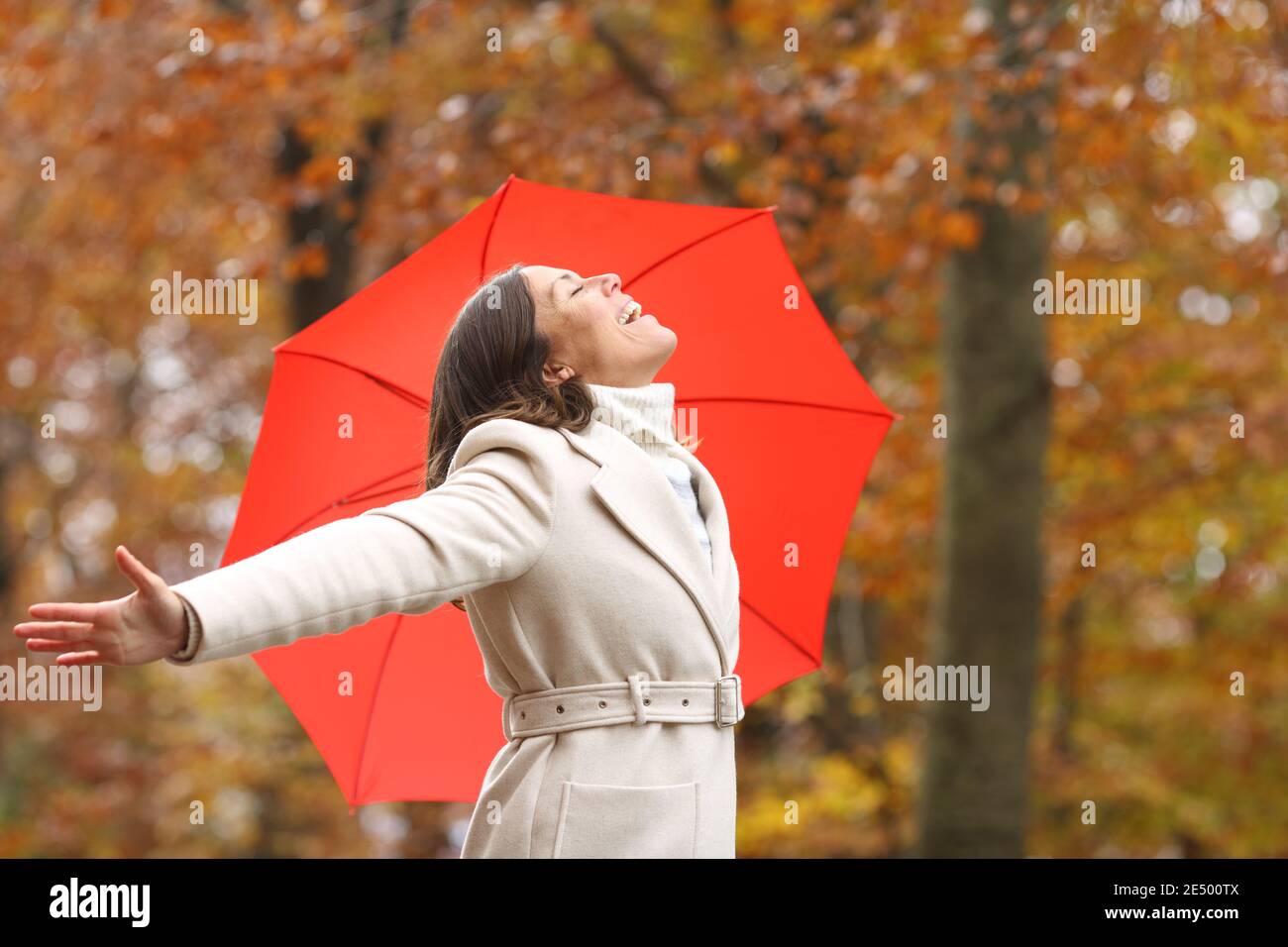 Glückliche Frau mittleren Alters atmen frische Luft im Winter mit Sonnenschirm in einem Park Stockfoto