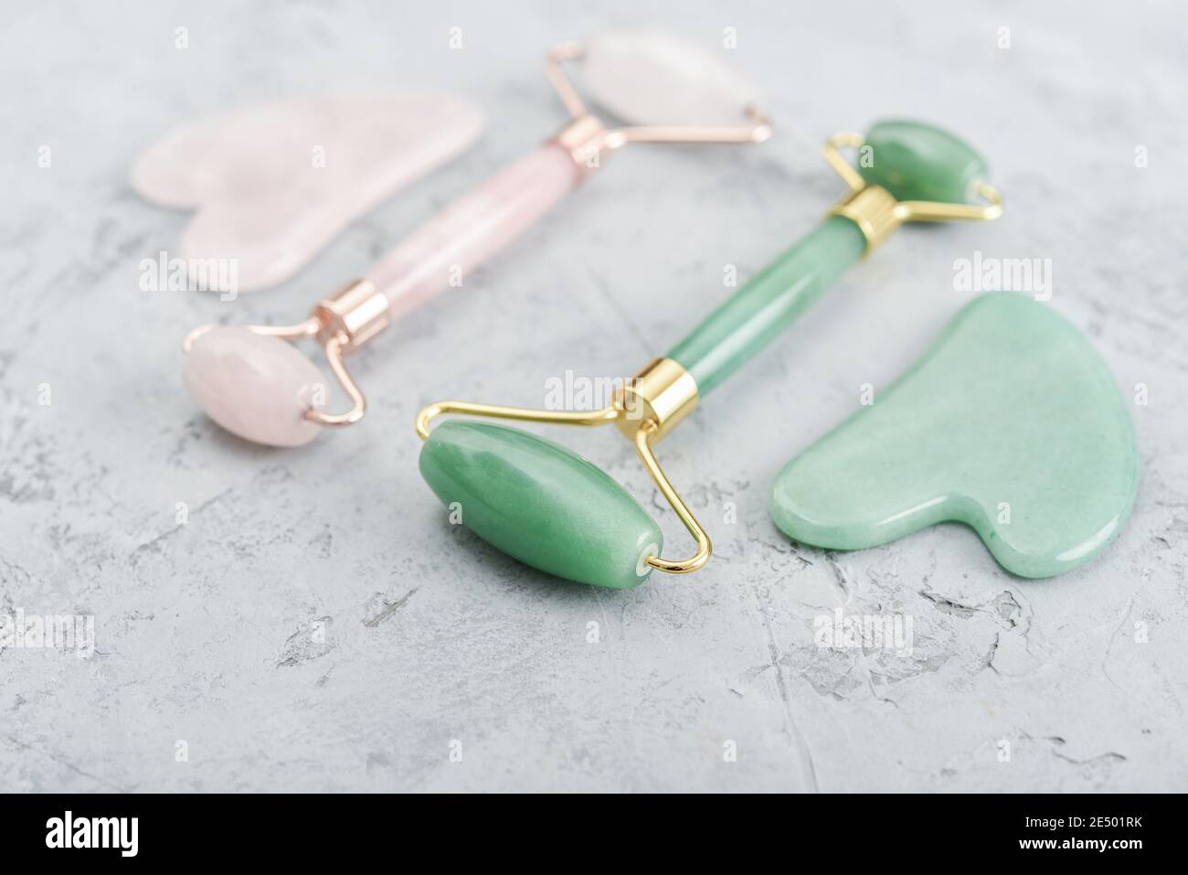 Gesichtsjade Massage Rollen und Gua Sha Massagegeräte aus gemacht Natürliche Jade und Rosenquarzstein auf grauem Hintergrund Stockfoto