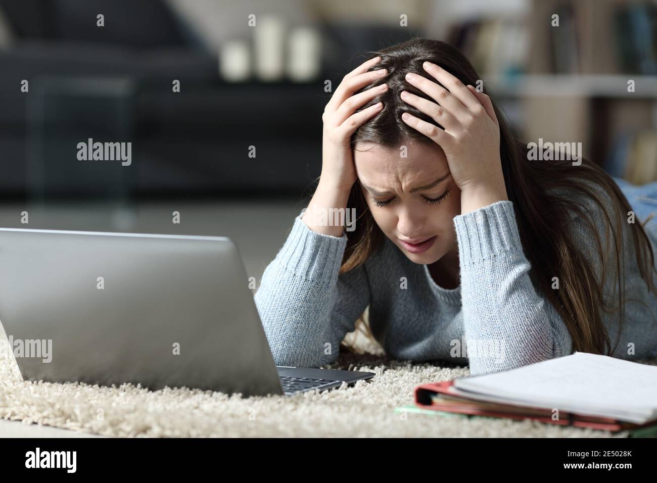 Traurige Studentin mit Laptop und Notebook, die sich beschwert, auf dem zu liegen Boden in der Nacht zu Hause Stockfoto