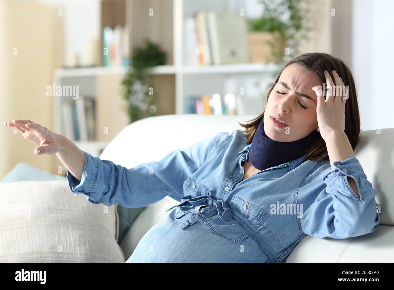 Schwindelerregende behinderte schwangere Frau mit Nackenstütze sitzt auf einem Couch im Wohnzimmer zu Hause Stockfoto