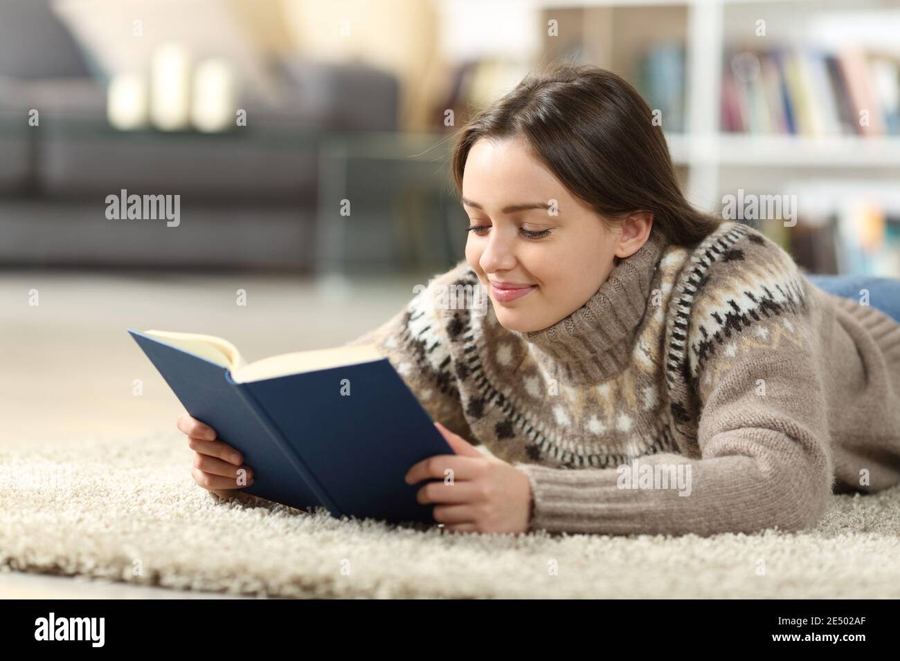 Zufrieden teen im Winter lesen Papier Buch liegt auf einem Teppich auf dem Boden im Wohnzimmer zu Hause Stockfoto