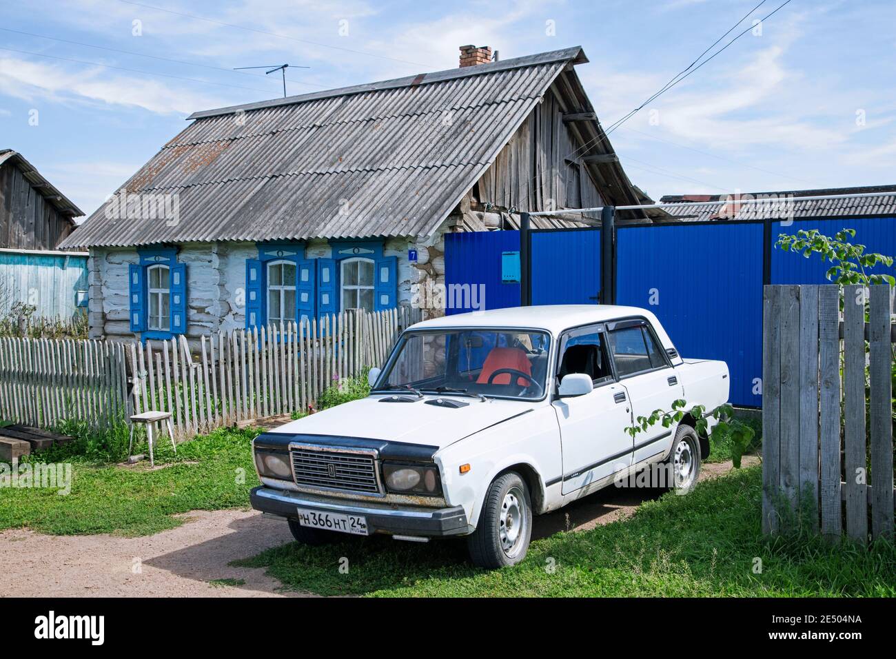 Traditionelles Holzhaus mit weißem Auto / Lada Riva / Lada Nova im ländlichen Dorf in Südsibirien, Russland Stockfoto