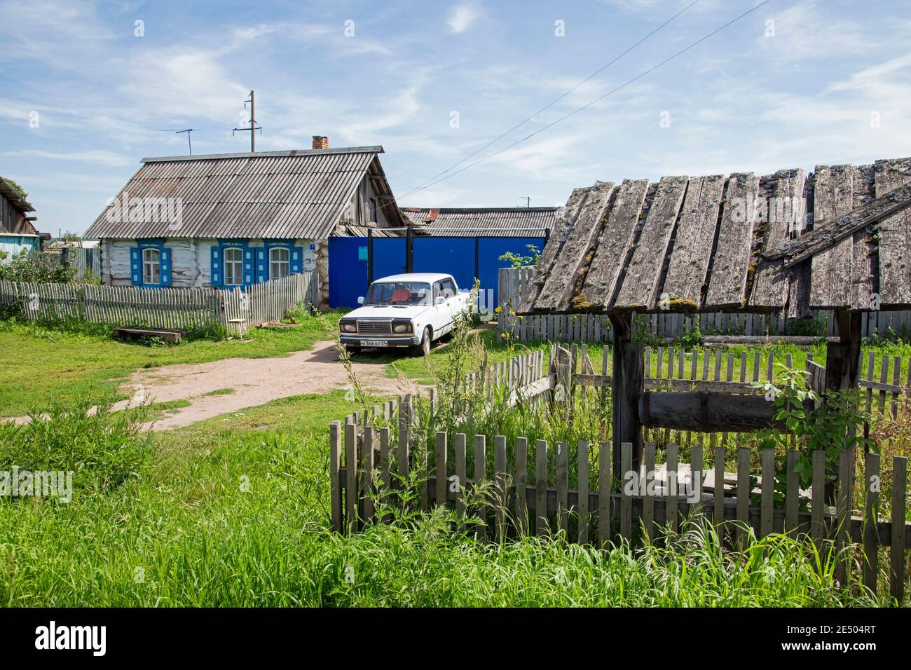 Traditionelles Holzhaus mit weißem Auto / Lada Riva / Lada Nova im ländlichen Dorf in Südsibirien, Russland Stockfoto