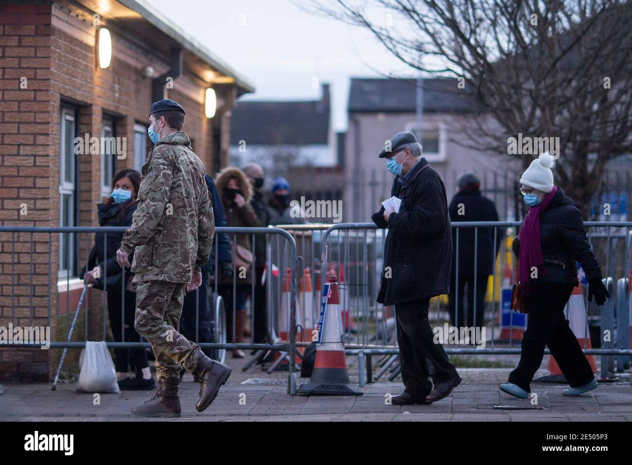 Cardiff, Wales, Großbritannien. Januar 2020. Ein Mann in Militäruniform führt ein älteres Paar an die Spitze einer Warteschlange für den Coronavirus-Impfstoff vor einem Impfzentrum im Gebiet Splott von Cardiff. Der walisische Gesundheitsminister Vaughan Gething sagte heute, es sei unklar, ob eine Zusage zur Impfung von 70 % der über 80-jährigen und in Pflegeheimen wohnenden Personen erreicht worden sei. Kredit: Mark Hawkins/Alamy Live Nachrichten Stockfoto