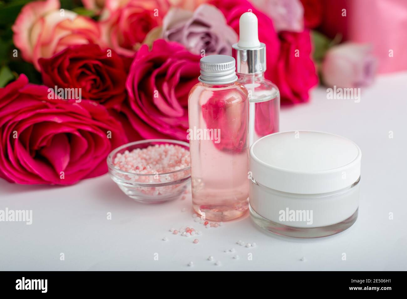 Glas Kosmetikflaschen, Creme, Serum, Seife, Öl auf weißem Tisch floralen Hintergrund. Blume rot rosa Rosen natürliche organische Schönheit Produkt. Spa, Hautpflege Stockfoto