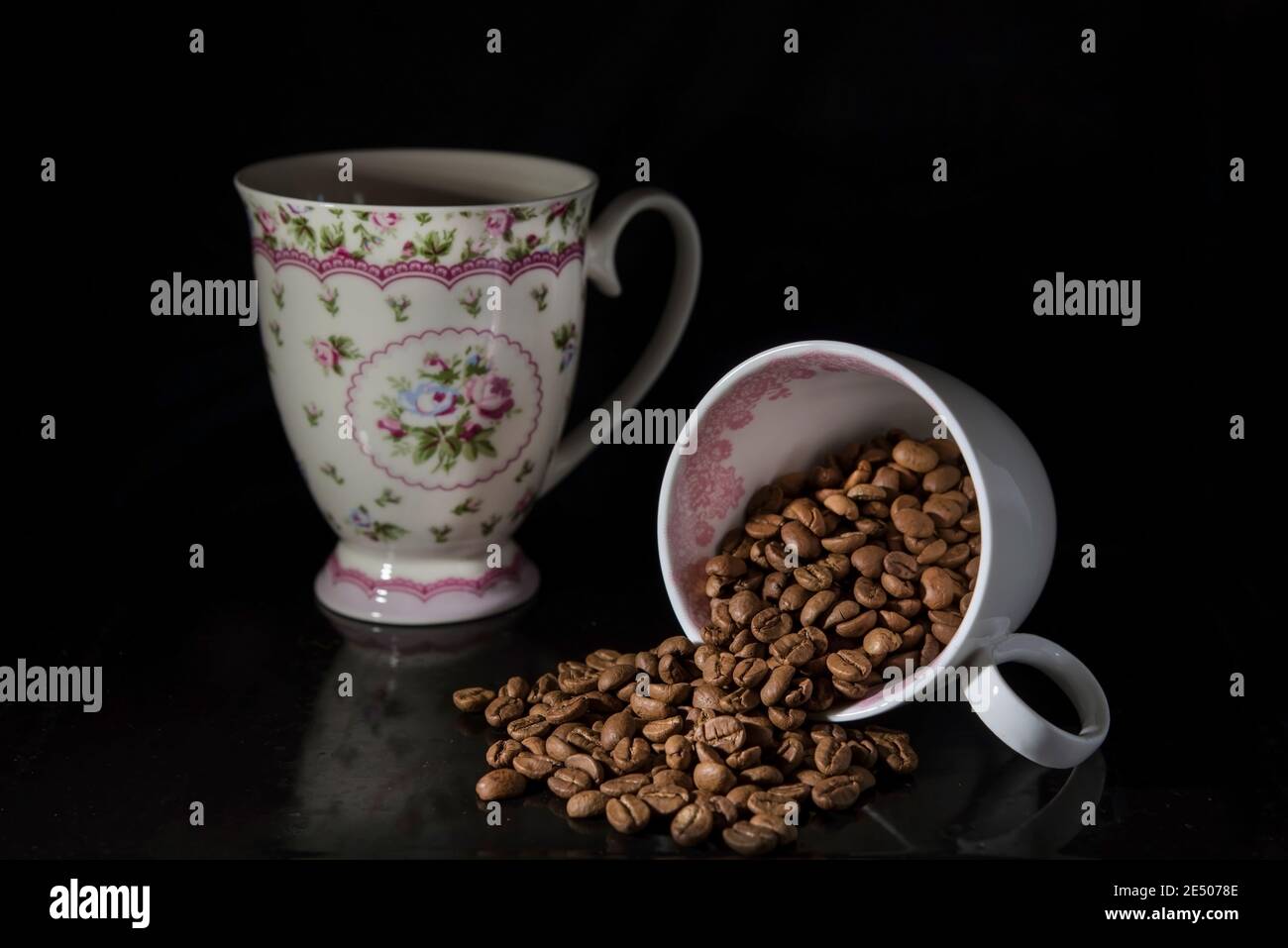 Ein Vintage-Becher und eine weiße Tasse Kaffee mit Bohnen auf schwarzem Hintergrund, isoliert, Nahaufnahme Stockfoto
