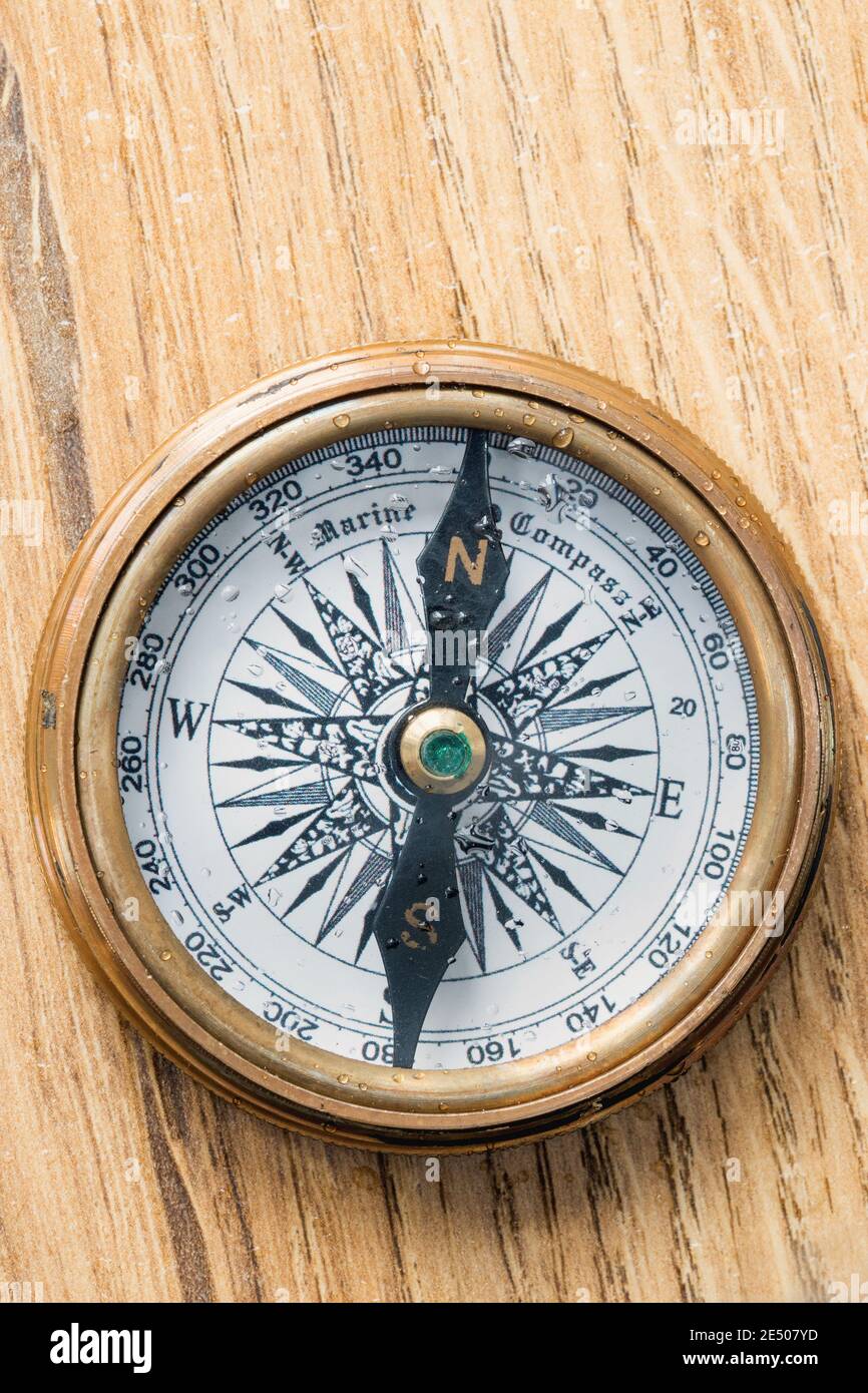 Altmodischer Kompass mit Wassertröpfchen bedeckt, der nach Norden zeigt Auf einer hölzernen Deckplatte Stockfoto