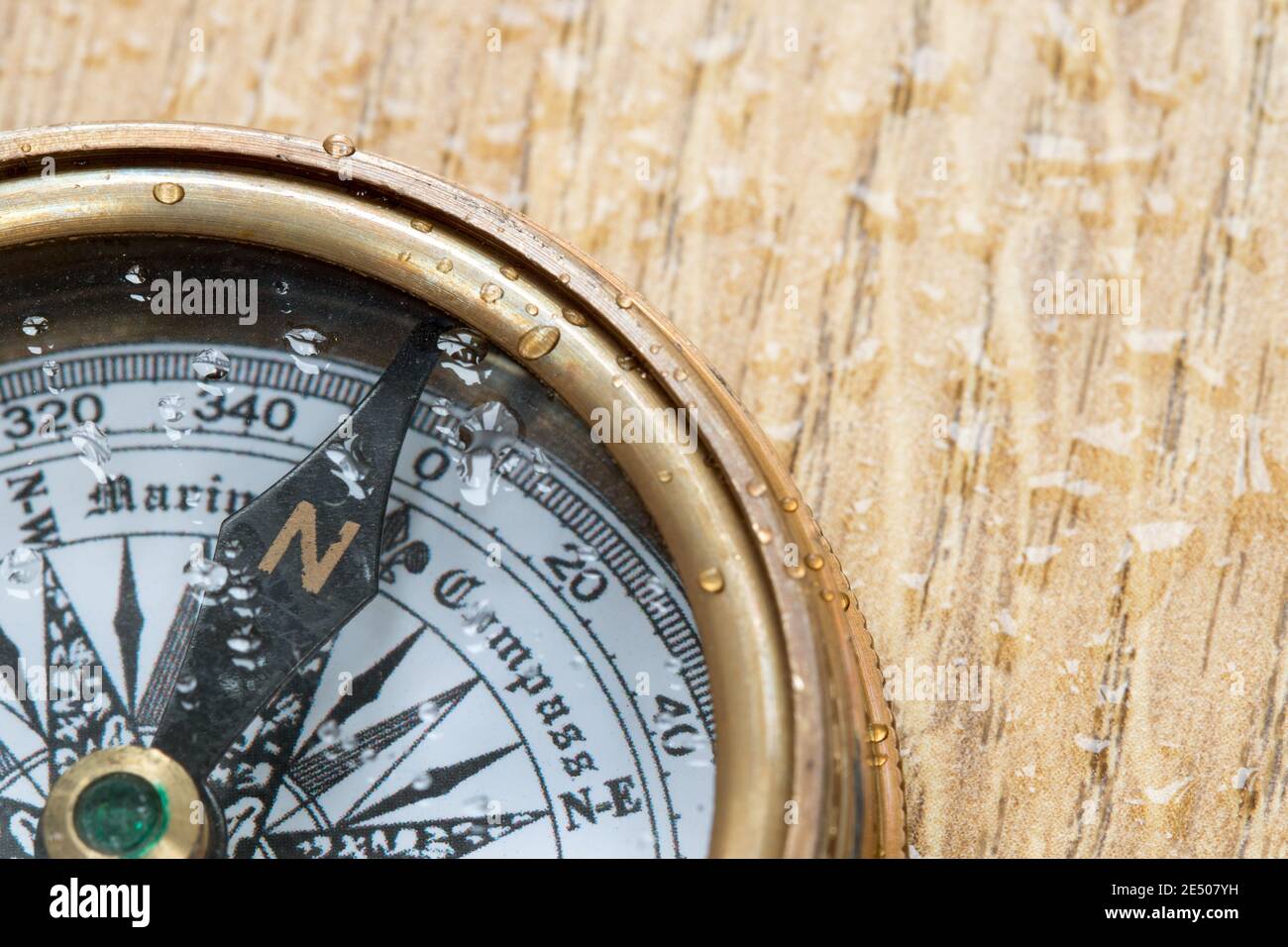 Altmodischer Kompass mit Wassertröpfchen bedeckt, der nach Norden zeigt Auf einer hölzernen Deckplatte Stockfoto