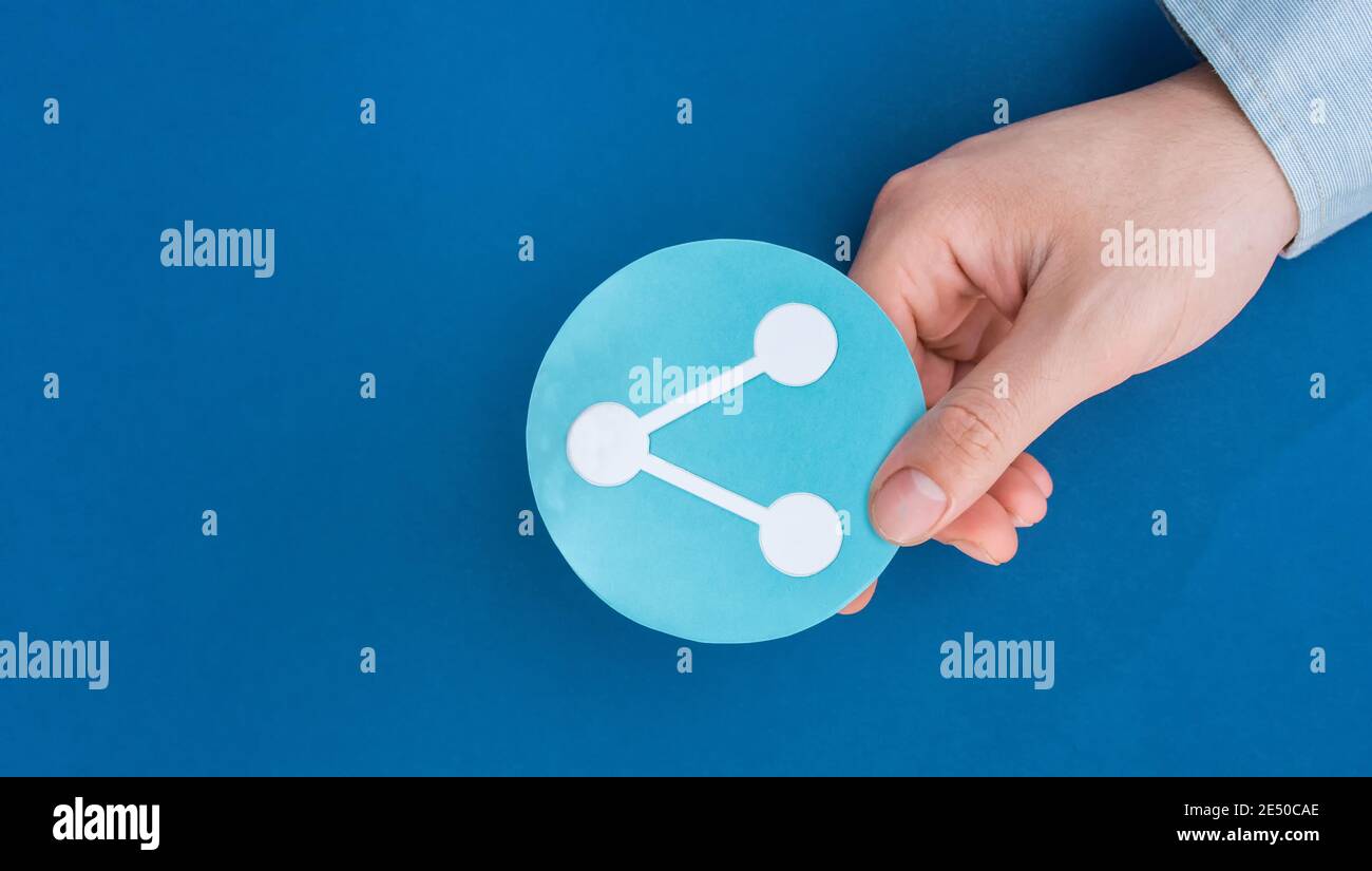 Nahaufnahme einer Person, die einen Ausschnitt aus einem Share Icon Papier hält Isoliert auf blauem Hintergrund Stockfoto
