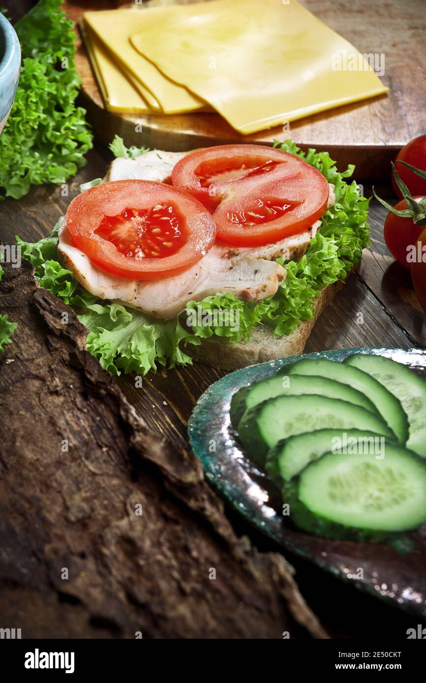 Leckeres Sandwich mit putenfleisch, frischen Tomaten, Gurken und grünem Salat, auf dunklem rustikalem Küchentisch, niemand Stockfoto