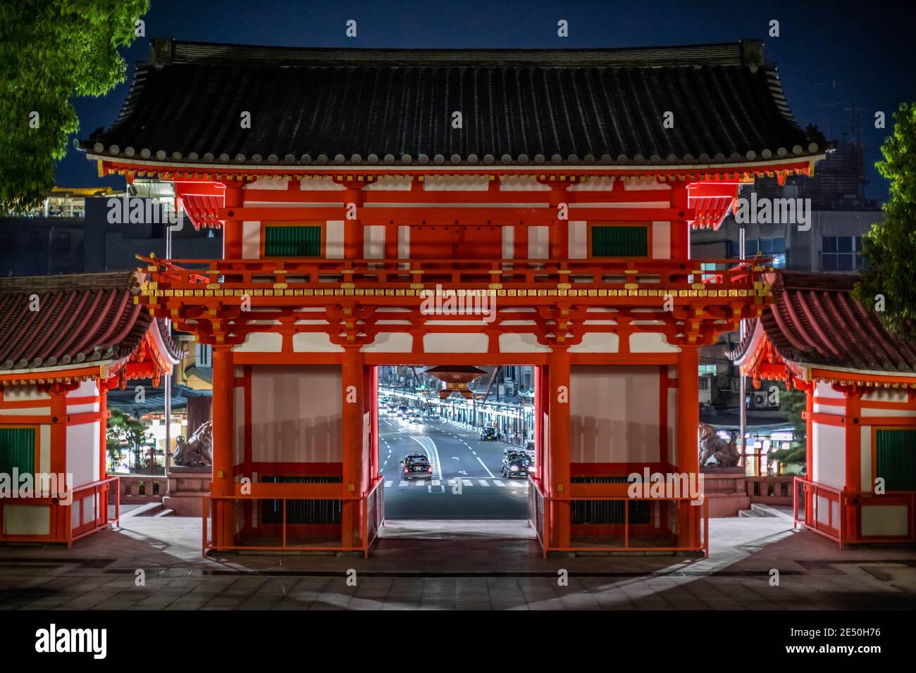 Symmetrische Nachtaufnahme eines roten japanischen Tempels, mit einer Straße und Stadtlichter im Hintergrund Stockfoto
