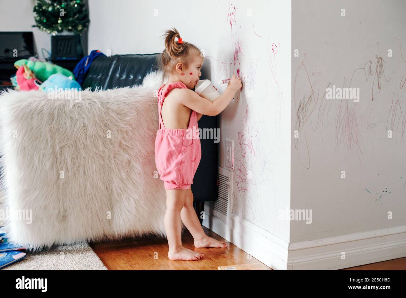 Lustige niedliche Baby-Mädchen Zeichnung mit Marker an der Wand zu Hause. Kleinkind Mädchen Kind mit Milchflasche spielen zu Hause. Authentische offene Kindheit Lebensstil Mo Stockfoto