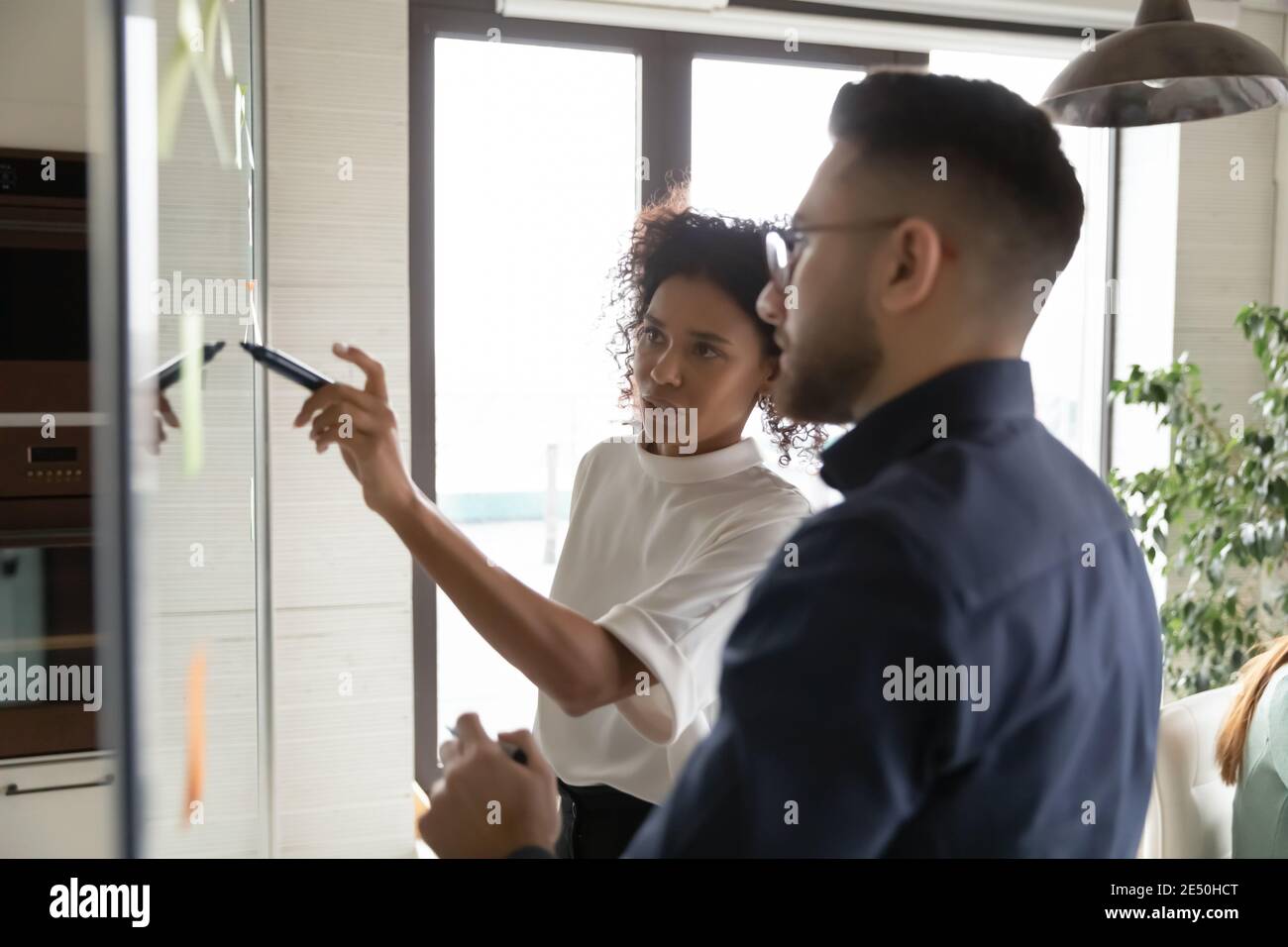 Nahaufnahme diverser Kollegen, die einen Plan entwickeln, auf Glaswand schreiben Stockfoto