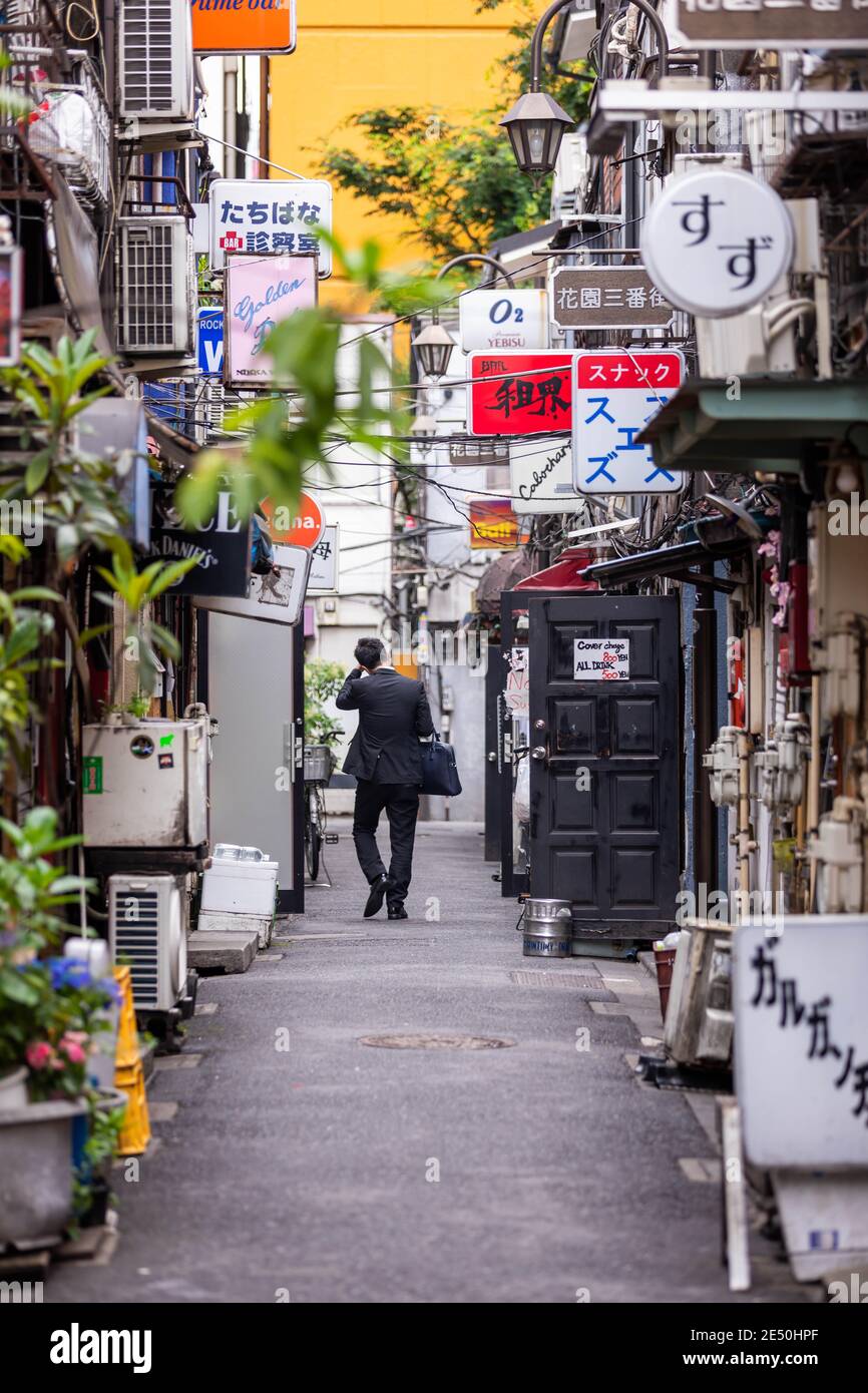 Nahaufnahme einer engen Hintergasse voller Restaurantschilder, mit einem Geschäftsmann, der einen Anzug trägt und am anderen Ende weggeht Stockfoto