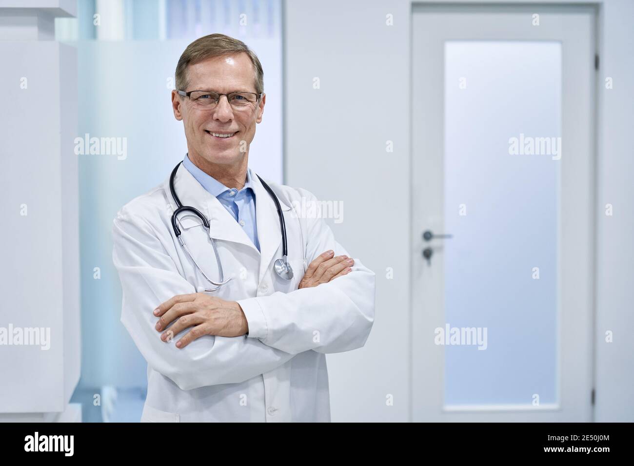Lächelnder reifer Oberarzt, der im Krankenhaus steht und die Kamera anschaut. Stockfoto