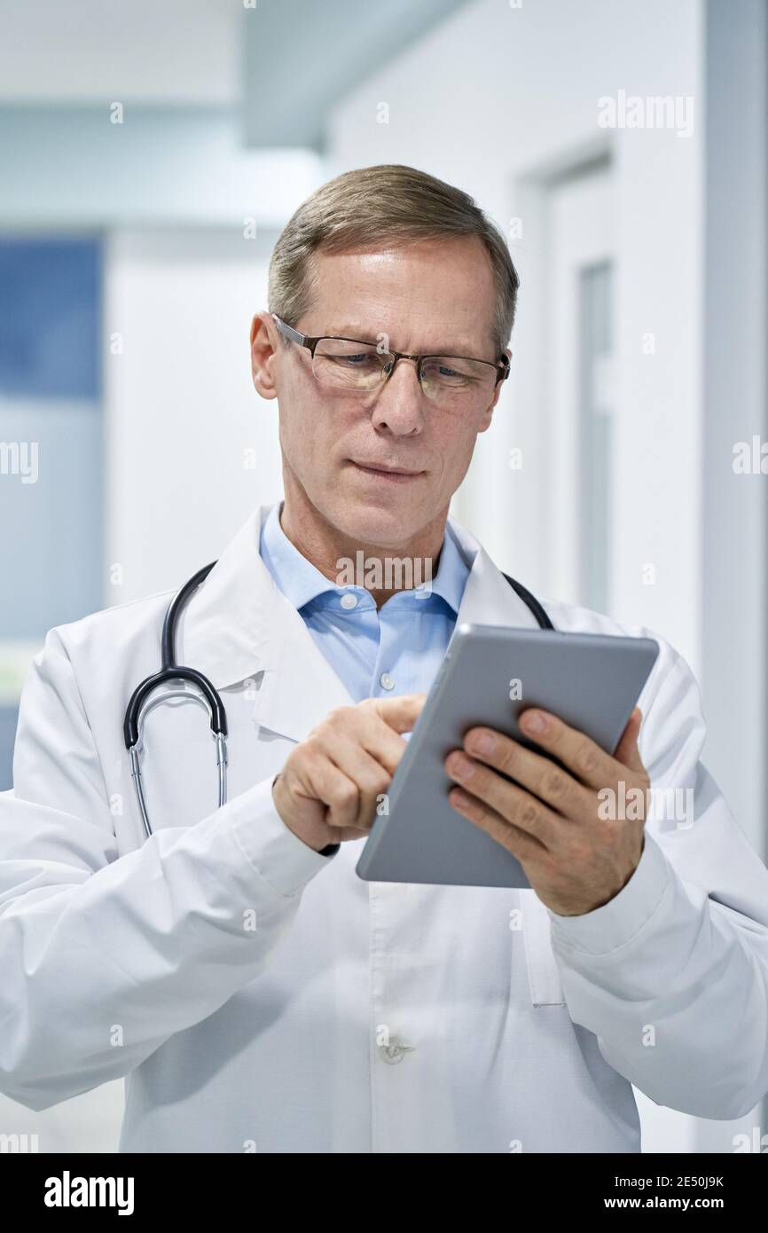 Reifer Arzt trägt eine Brille mit digitalen Tablet im Krankenhaus. Stockfoto