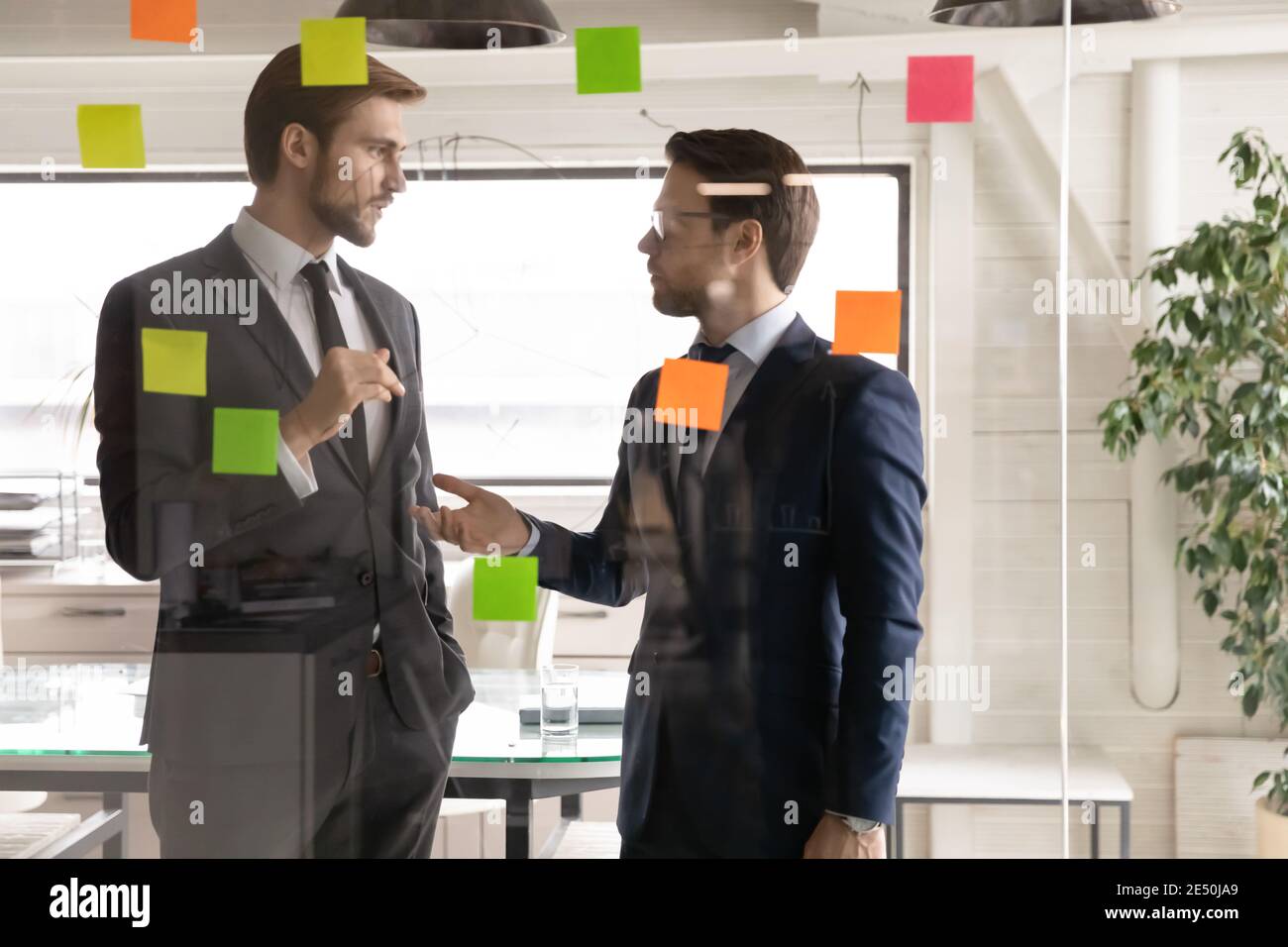 Kollegen diskutieren Projektstrategie, stehen neben Glaswand mit Aufklebern Stockfoto