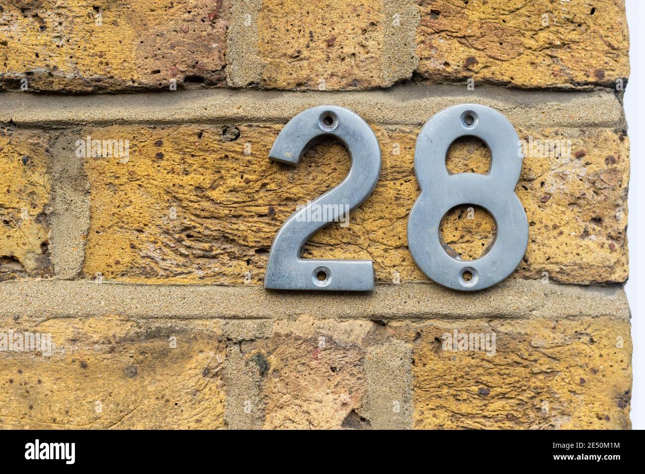 28 als glänzende Metallziffern auf einem rohen gelben Ziegel Wand Stockfoto