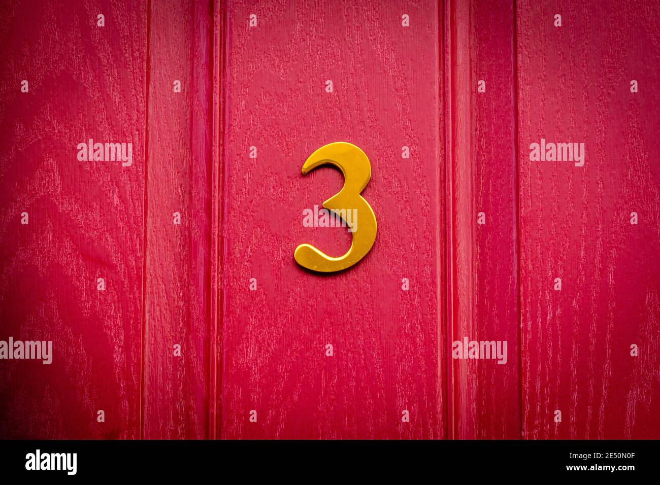Goldene Nummer 3 auf einer roten Holztür mit Dunkle Ecken Stockfoto