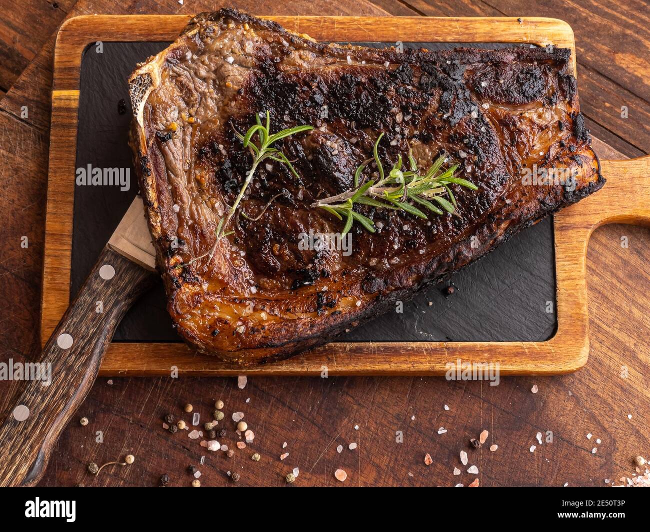 Gegrilltes sashi-Rindersteak mit Rosmarin, schwarzem Pfeffer, himalaya-Salz und einem Messer auf einem Holzbrett Stockfoto