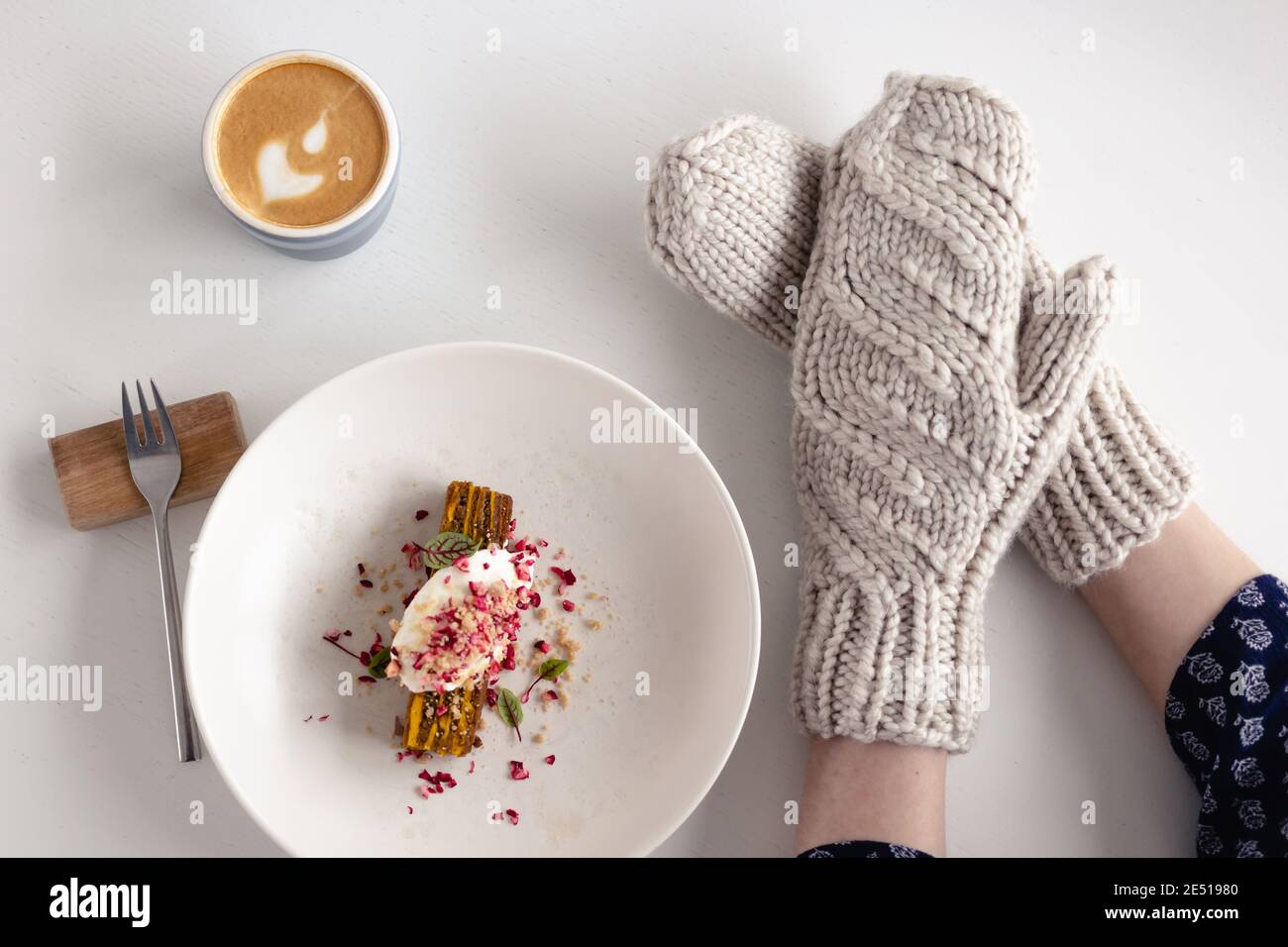 Weibliche Hände in weißen Fäustlingen mit Kuchen und Kaffee auf weißem Tisch mit Kuchen. Konzept von Winter, Wärme, Urlaub, Veranstaltungen. Stockfoto