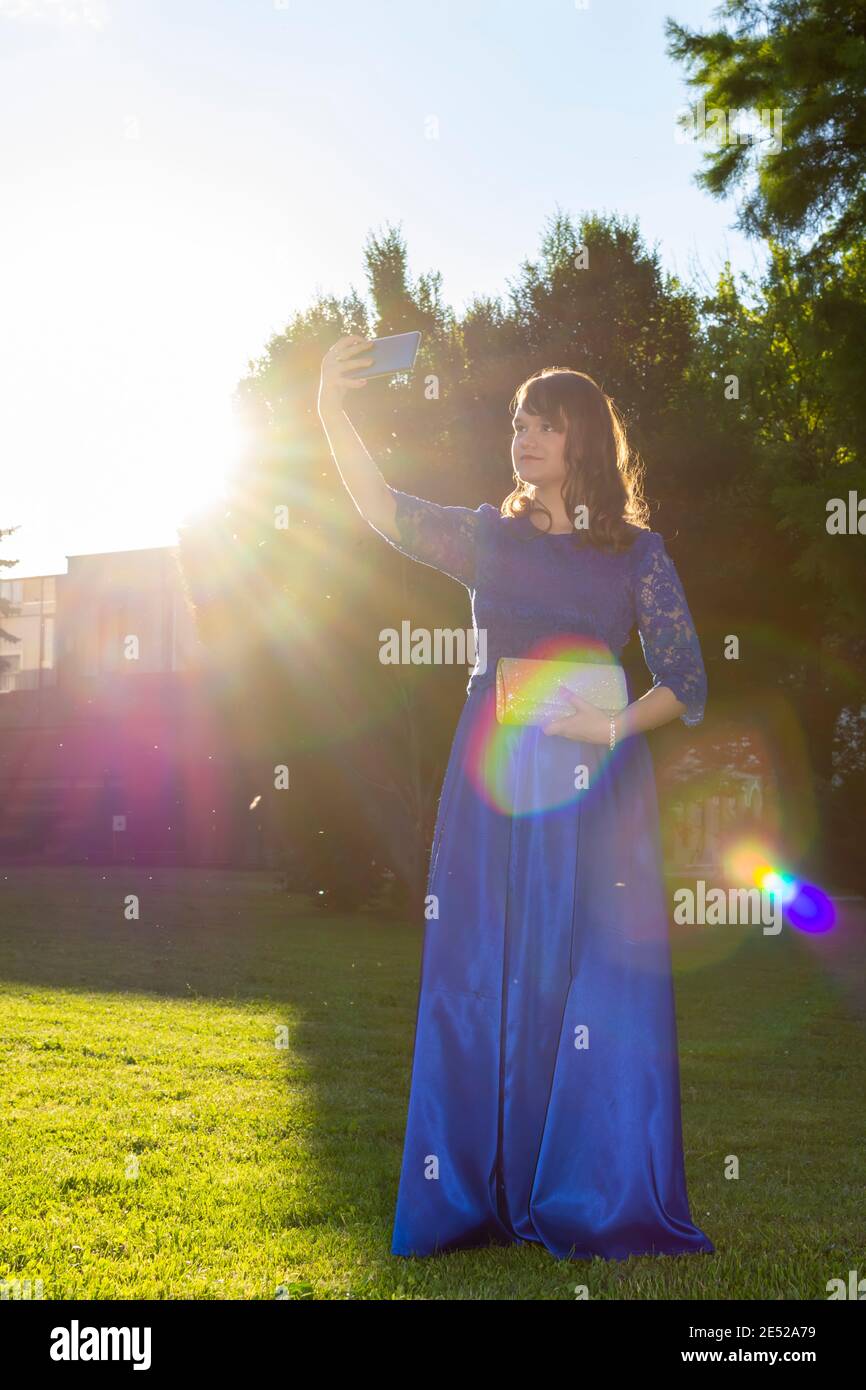 Schöne lächelnde weibliche Modell in elegantem Kleid unter Selfie im Sommer Park. Liebenswert modische Mädchen in blauem Outfit in der Natur. Kunstfoto. Auswahl Stockfoto