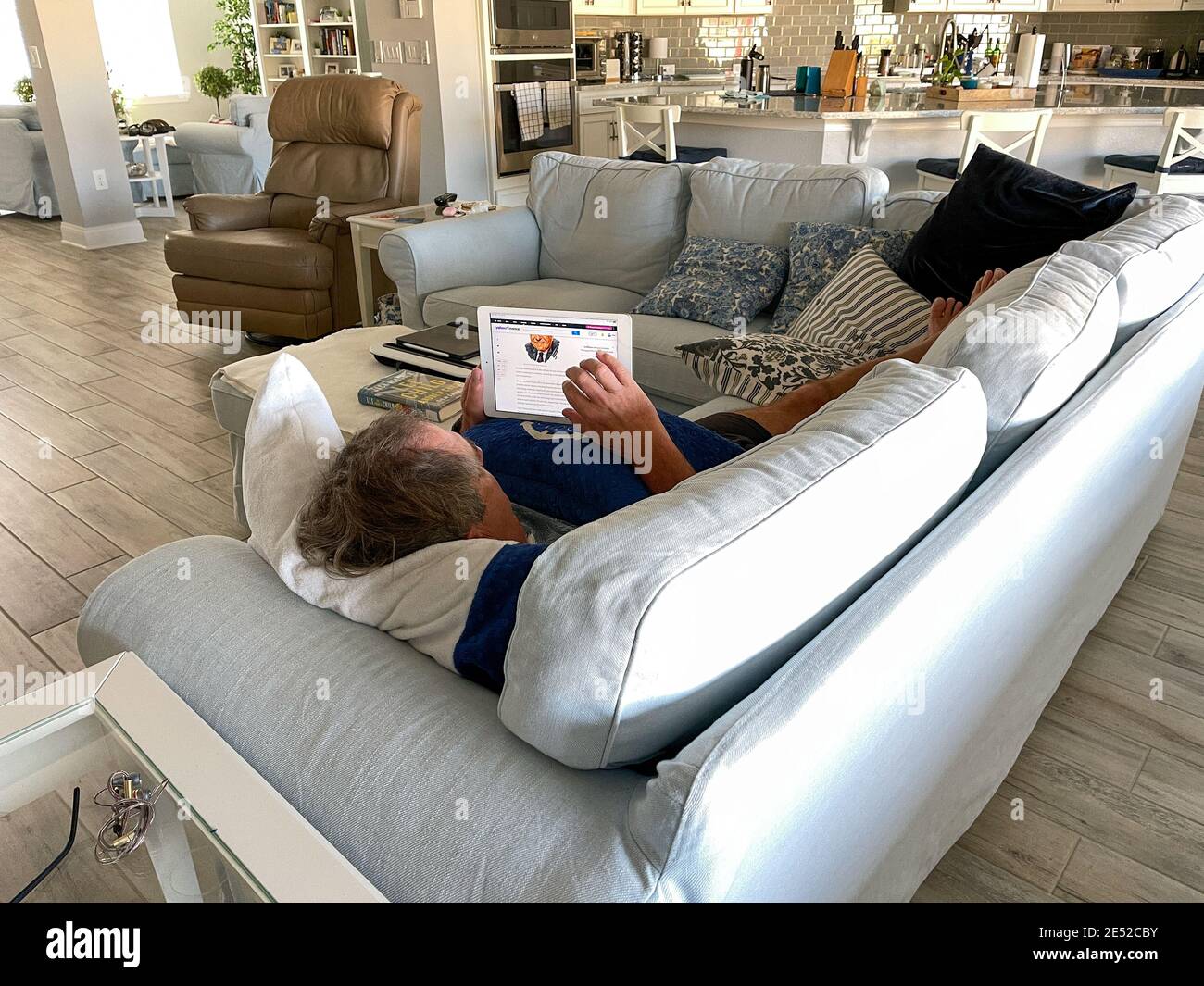 Orlando, FL USA - 25. Januar 2021: Ein älterer Mann liest die Nachrichten auf seinem iPad, während er auf der Couch liegt. Stockfoto